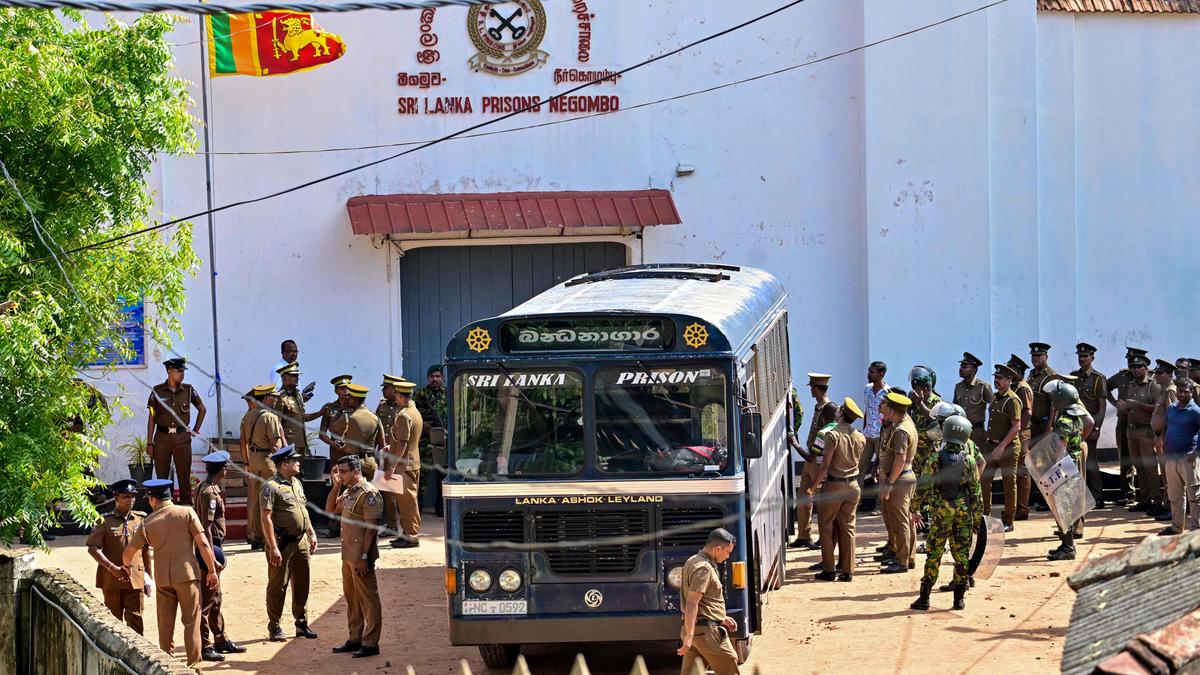 Exterior of a prison complex with police vehicles and a government building in the background